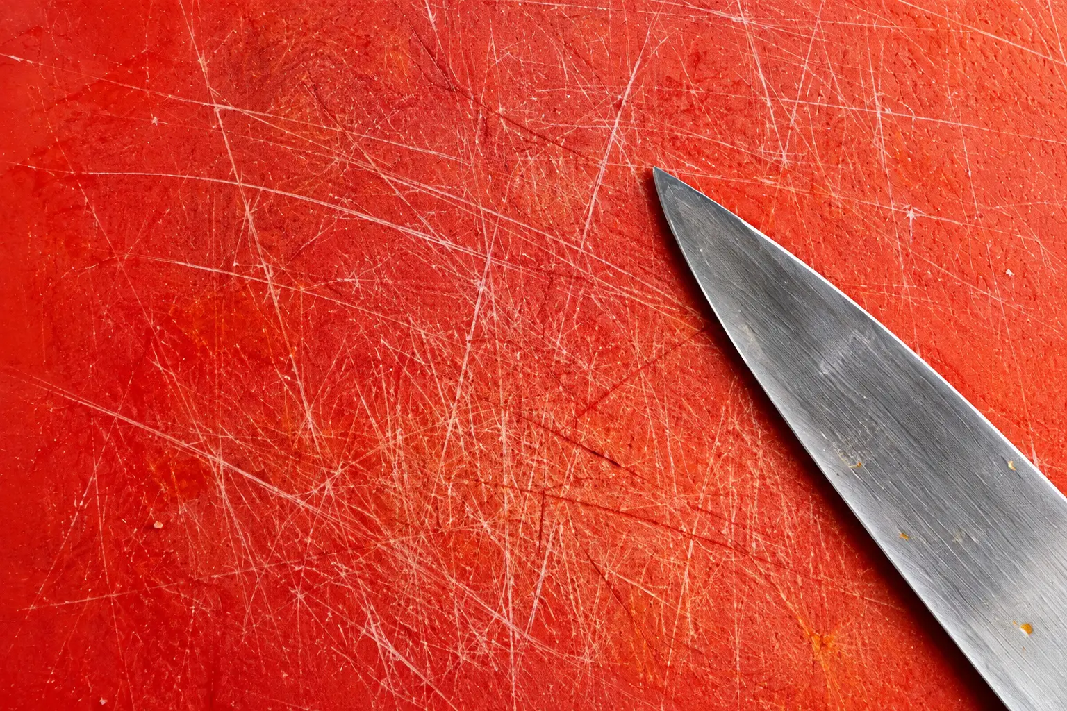 A heavily scratched red plastic cutting board covered in deep knife cuts, with a chef's knife resting on it
